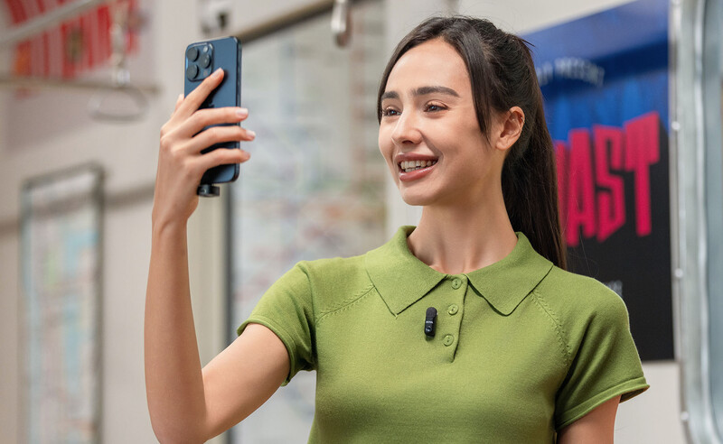 Woman in green polo shirt holding smartphone while smiling, photographing in retail environment.
