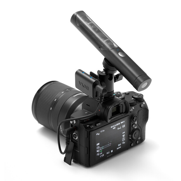 Professional video camera with attached shotgun microphone and zoom lens mounted on shoulder rig.