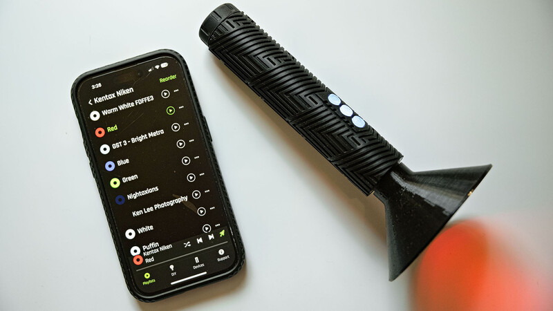 Smartphone displaying audio editing app interface next to a black condenser microphone and orange diffuser.