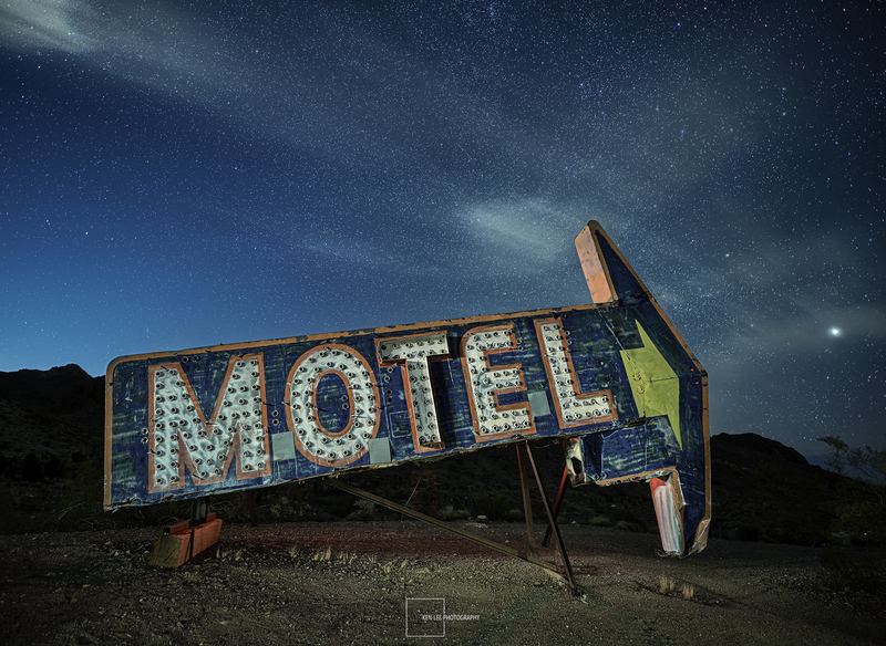 Abandoned motel sign illuminated at night under a starry sky with dramatic clouds.