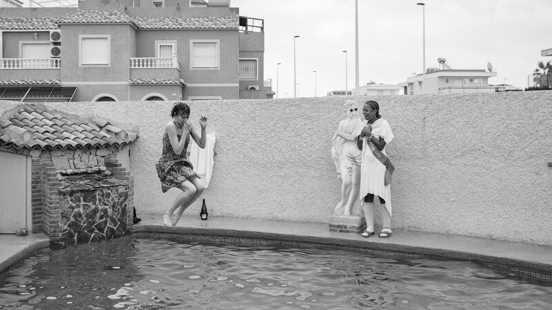 Two women posed at opposite ends of a residential swimming pool in a black and white photograph.