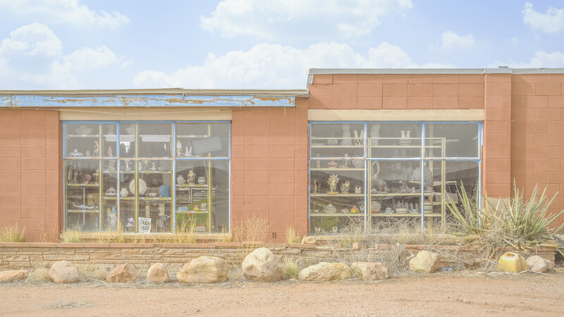 Abandoned retail storefront with terracotta brick facade and large display windows containing shelves of merchandise.