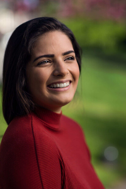 Woman in red shirt smiling at camera with blurred green background.