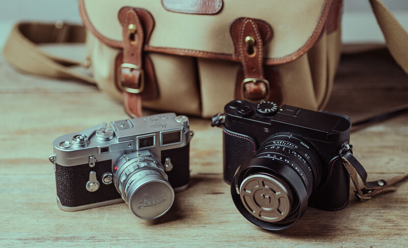 Two vintage rangefinder cameras with leather carrying bag on wooden surface.