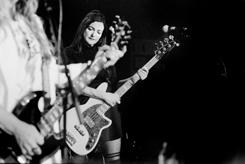 Female guitarist performing on stage with electric guitar, captured in black and white during live performance.