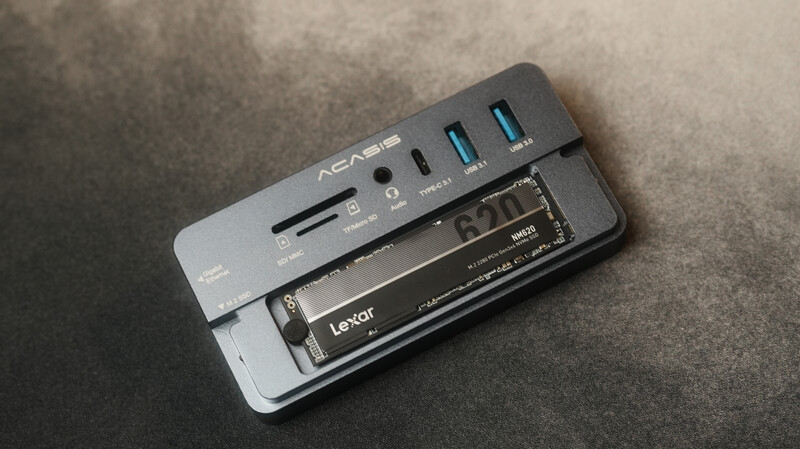 Acasis card reader and USB hub with Lexar memory card inserted, showing multiple USB ports and SD card slot on gray surface.