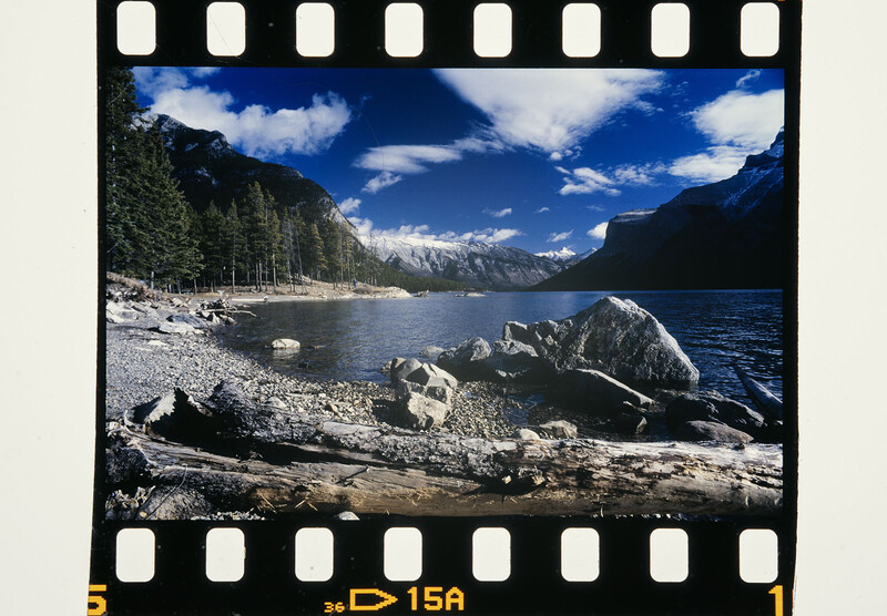 Alpine lake surrounded by mountains with rocky shoreline and evergreen forest under blue sky.