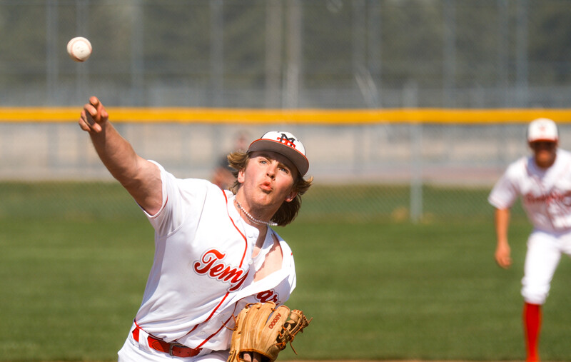 Baseball player in mid-throw, focused upward at an incoming ball during a sunny game.