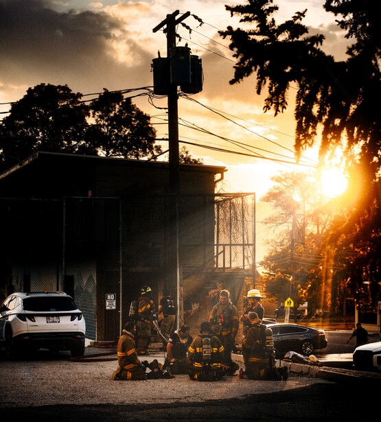 Silhouetted figures gathered outside an industrial building at golden hour sunset.