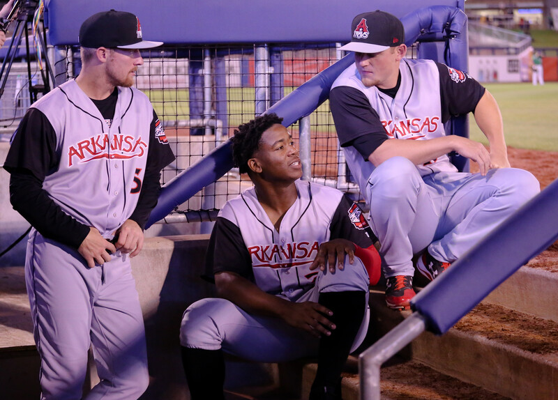 Three baseball players in dugout during game, sitting together on bench.