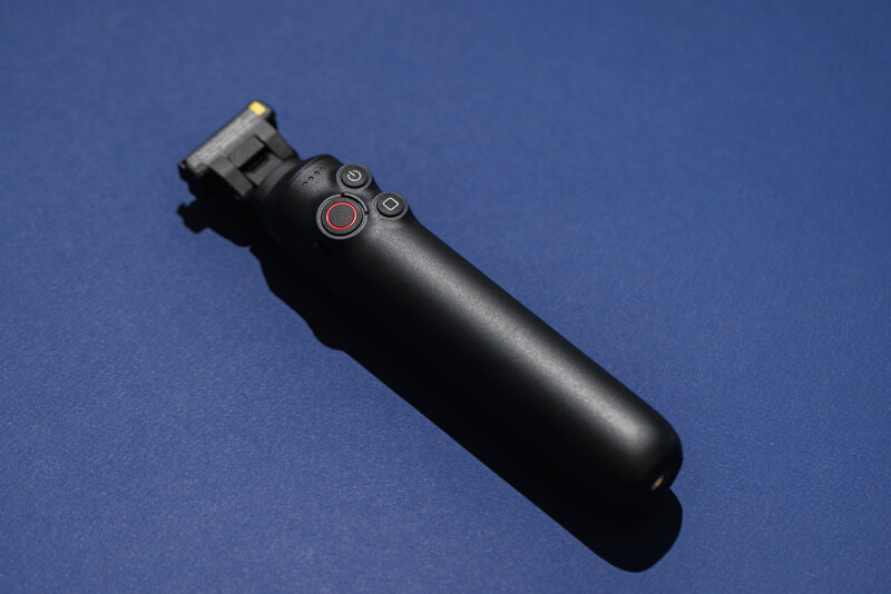 Black handheld gimbal stabilizer with mounting bracket and control buttons on blue background.
