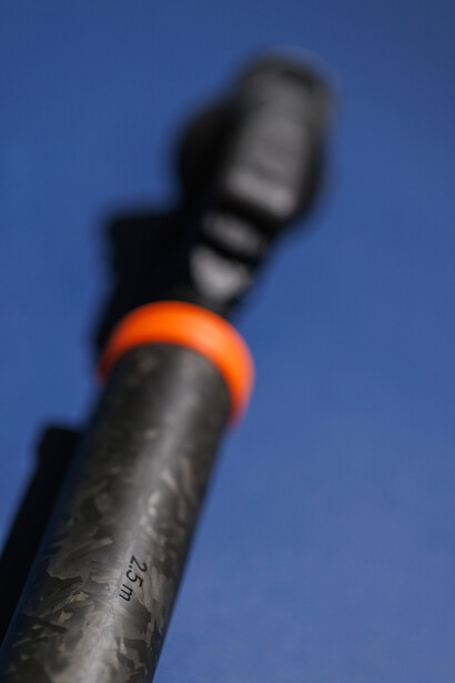 Close-up of a rope with an orange carabiner clip against a clear blue sky.
