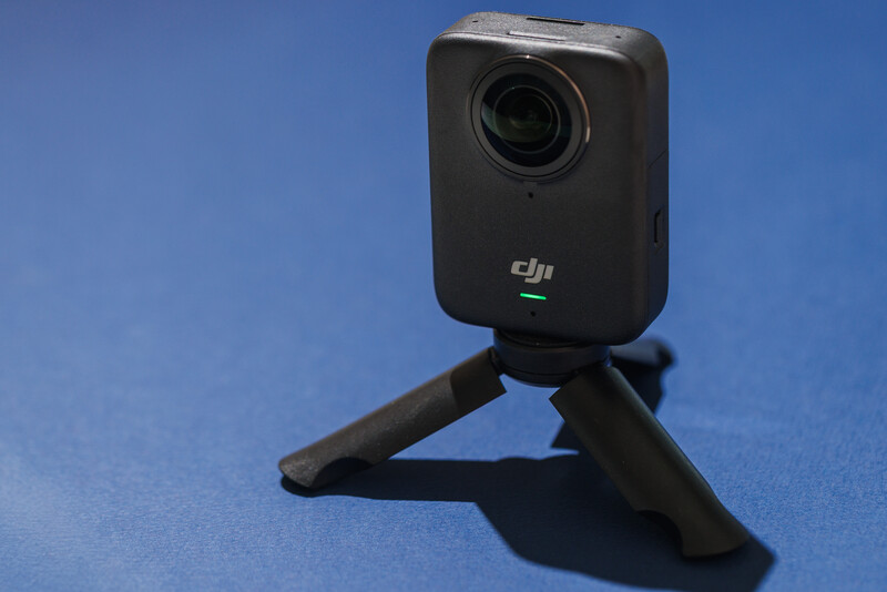 DJI Osmo Pocket compact action camera mounted on its tripod stand against a blue background.