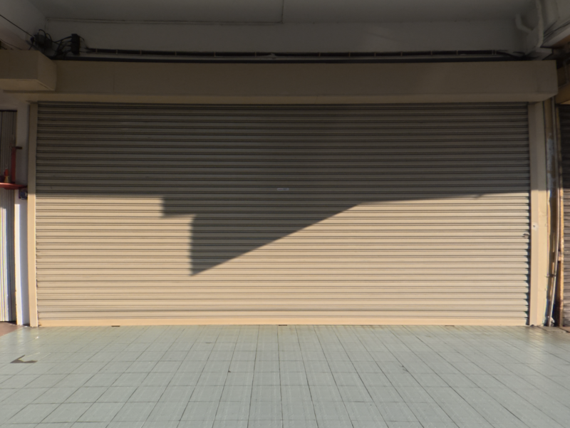 Empty garage interior with closed roller shutter door and afternoon shadow cast across cream-colored wall.