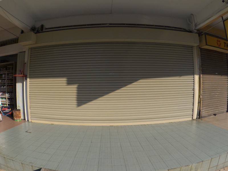 Empty storefront with closed metal rolling shutter in bright afternoon sunlight.