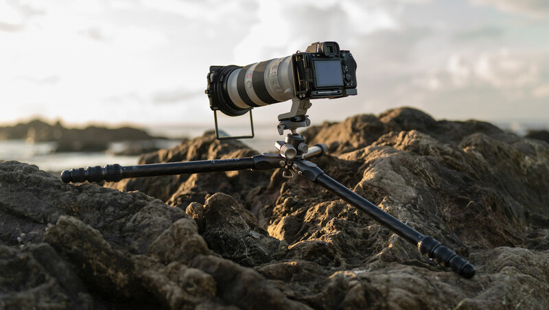DSLR camera with telephoto lens mounted on tripod positioned on rocky coastal terrain.