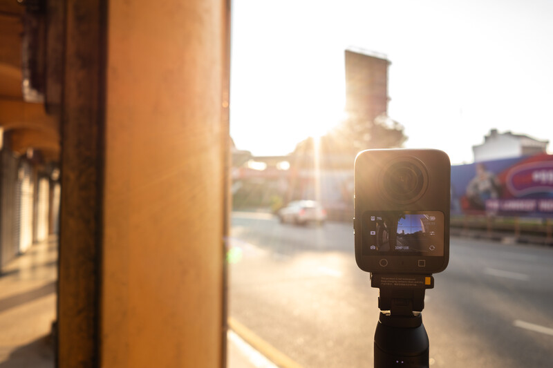 Compact camera mounted on tripod during golden hour with blurred street scene in background.