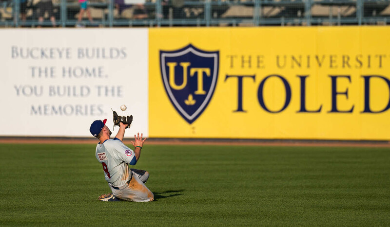Baseball player sliding on outfield grass while catching a fly ball.