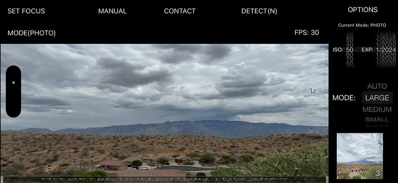 Screenshot of smartphone camera interface showing a desert landscape with mountains and storm clouds.