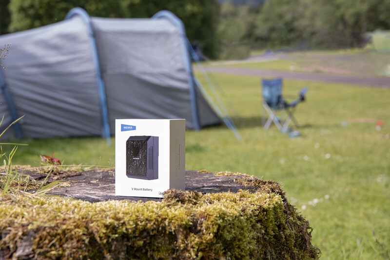 Packaged camping heater displayed on moss-covered log with tent and camping chair blurred in background.