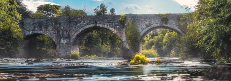 Historic stone arch bridge spanning a river surrounded by dense green foliage.