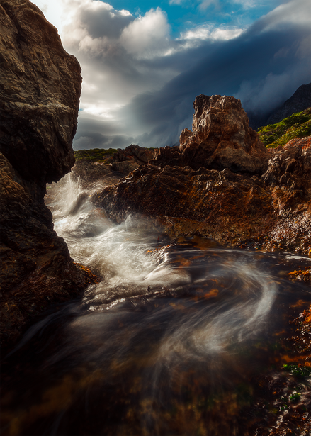 Turbulent river flowing through rocky terrain beneath dramatic cloudy sky.