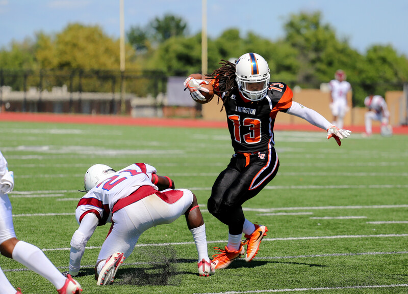 Youth football player in black and orange uniform evading defender in red and white uniform during a game.