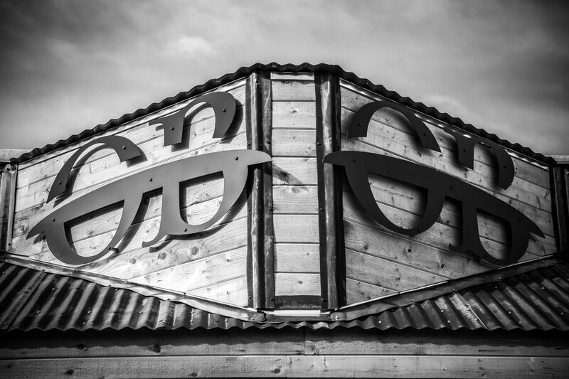 Black and white photograph of architectural metal framework with curved decorative elements and corrugated metal panels.