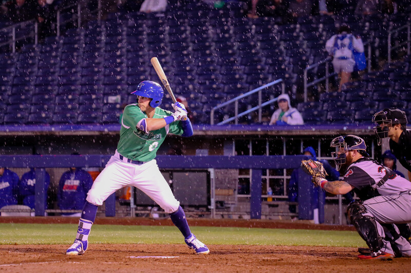 Baseball batter in green uniform at bat during night game under stadium lights.