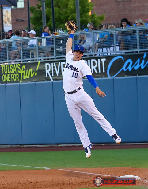 Baseball player in white uniform jumping to catch a ball in outfield during daytime game.