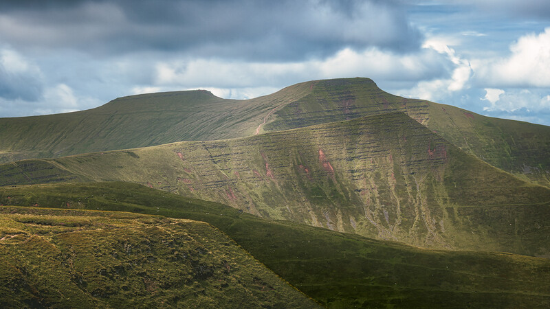 Layered mountain with moss-covered slopes and exposed geological strata under dramatic cloudy sky.