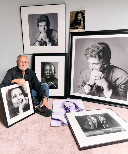 Photographer posing with collection of framed black and white portrait prints and contact sheets.