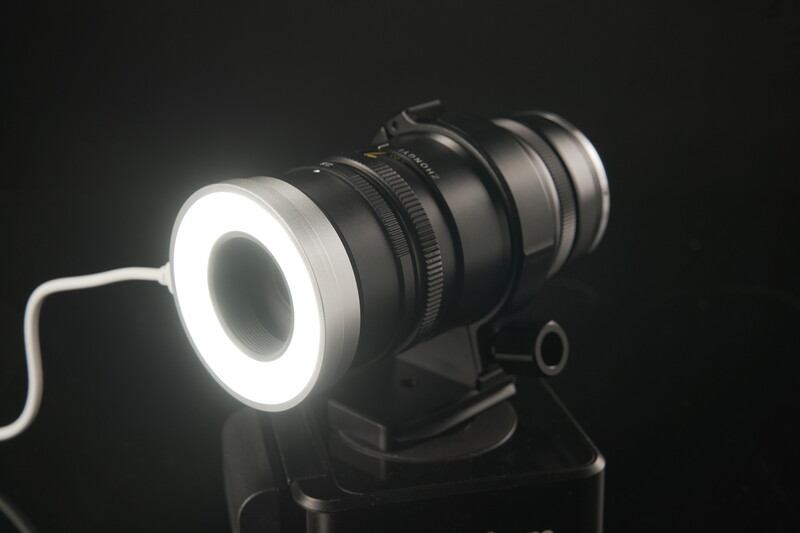 Macro ring light with illuminated LED circle mounted on camera lens against dark background.