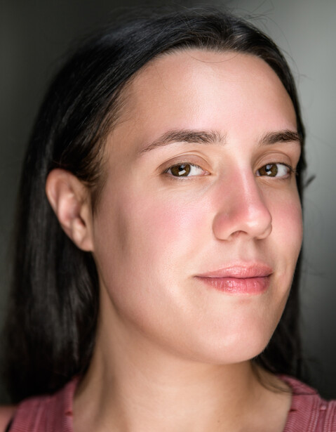 Portrait of a person with long dark hair and neutral expression against a gray background.