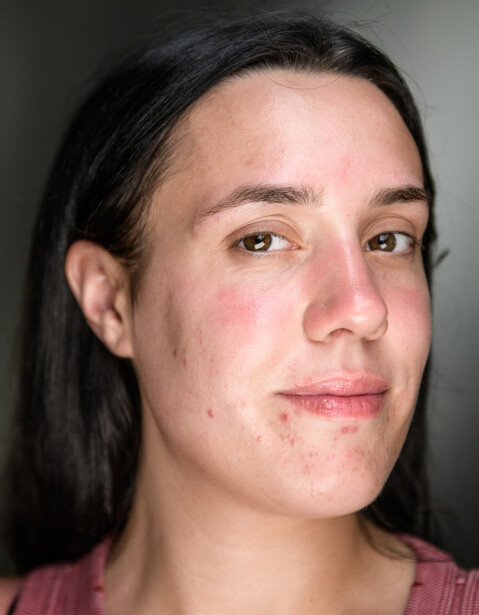 Close-up portrait of a person with long dark hair against a neutral gray background.