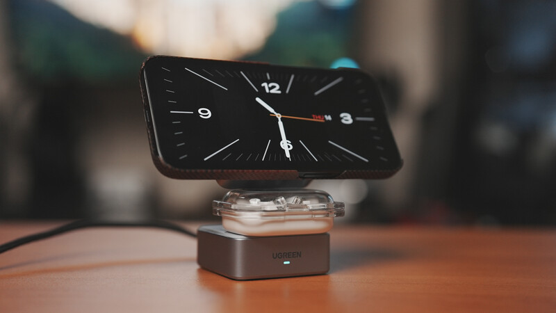 Smartphone displaying a black analog clock face mounted on a small wooden stand with cable.