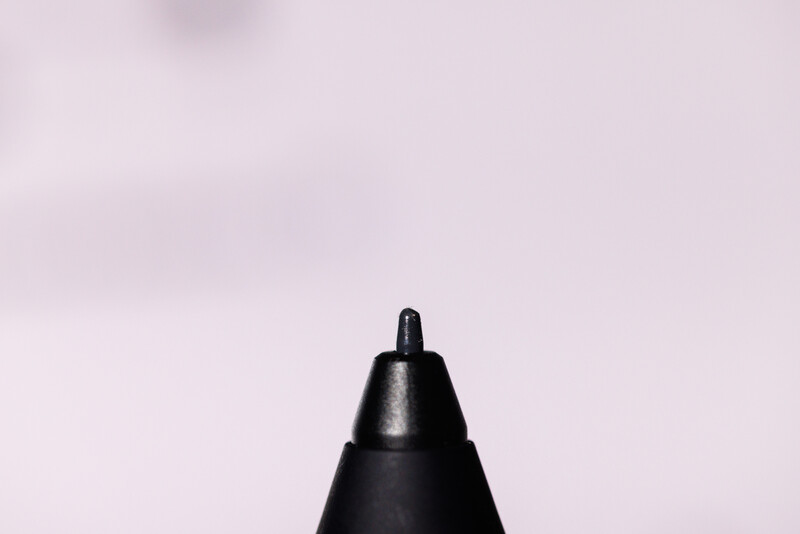 Macro photograph of a black pen tip against a soft pink background.