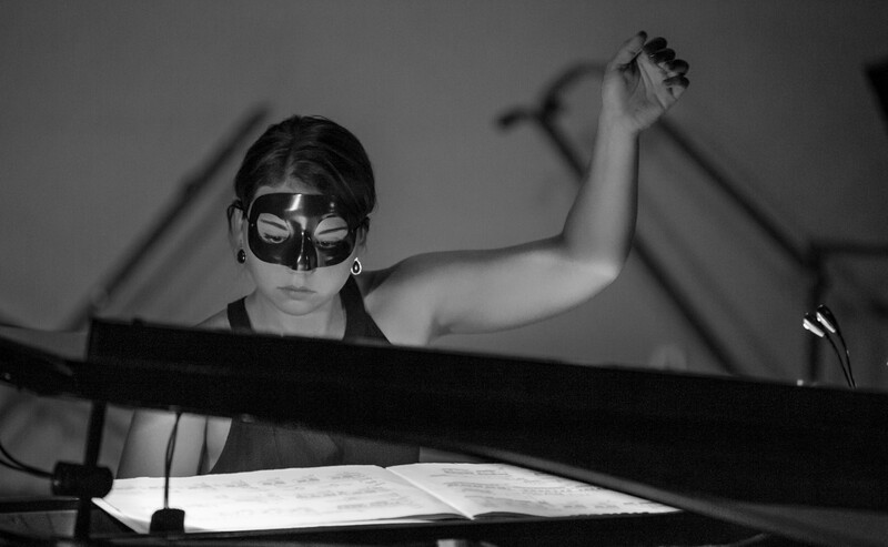 Musician wearing a decorative face mask performing at a piano in black and white.