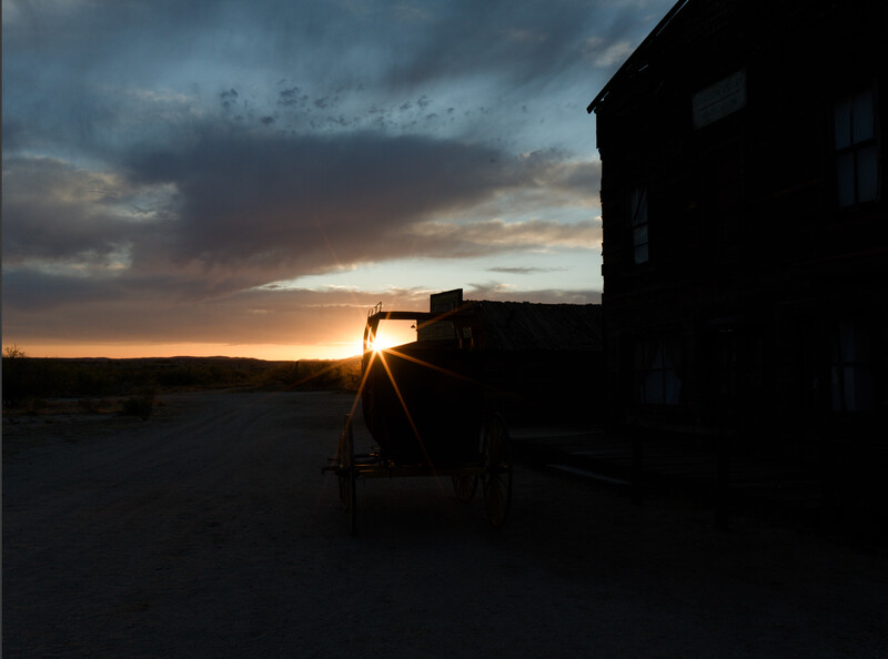 Silhouetted film camera on tripod backlit by dramatic sunset sky with storm clouds.
