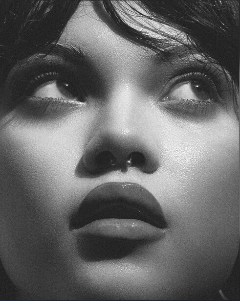 Black and white portrait of a person with dramatic upward gaze and strong overhead lighting creating deep shadows.