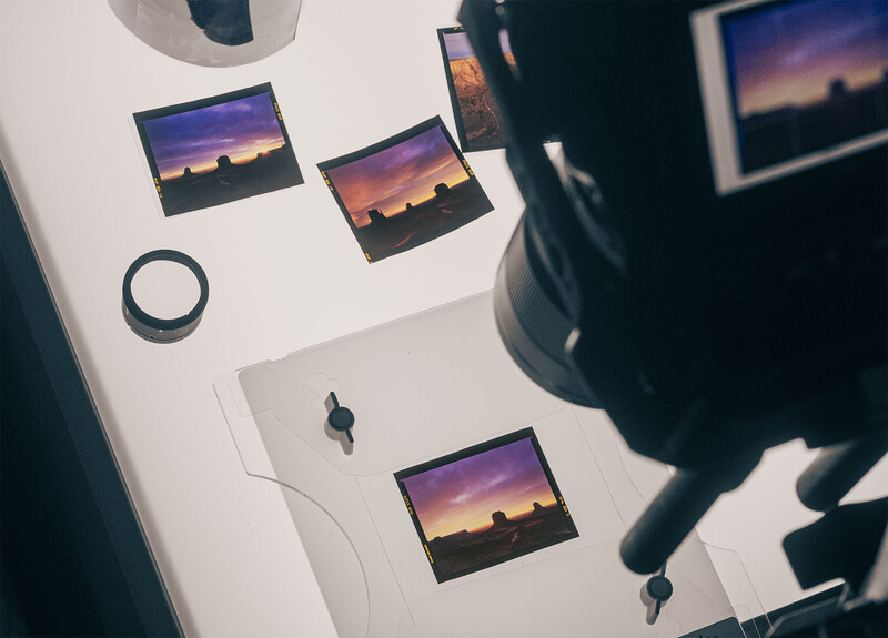 Overhead view of printed photos and photography equipment arranged on white surface with camera lens visible.