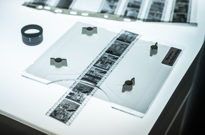 Vintage film negatives, enlarger lens, and optical equipment arranged on a light table.