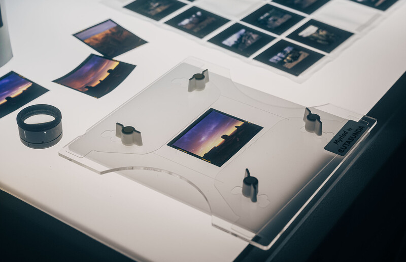 Flat lay of photography equipment and prints arranged on a white surface, including earbuds, cables, and landscape photographs.