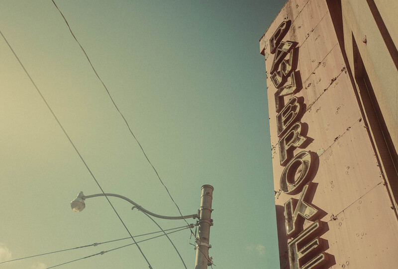 Vintage neon sign mounted on brick building with power lines and clear sky.