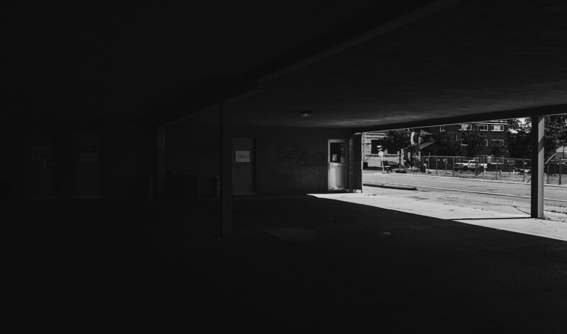 Dark interior storefront with bright daylight streaming through large windows, revealing an empty street outside.