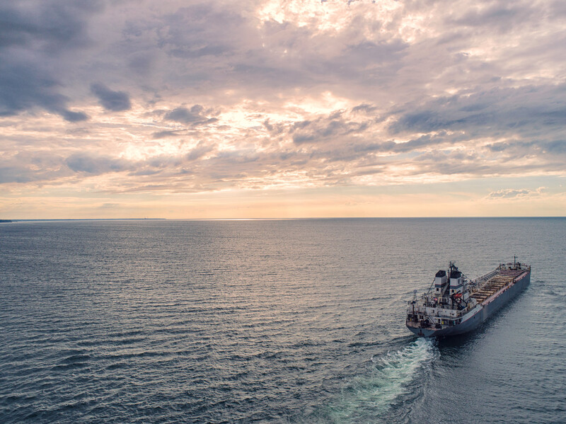 Large industrial tanker ship sailing across calm ocean waters under dramatic cloudy sky.
