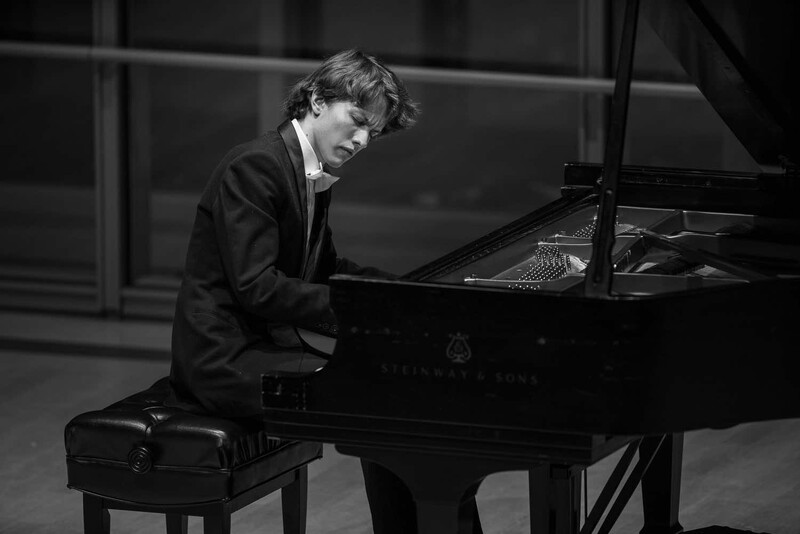 Young pianist in formal attire performing at grand piano in black and white.