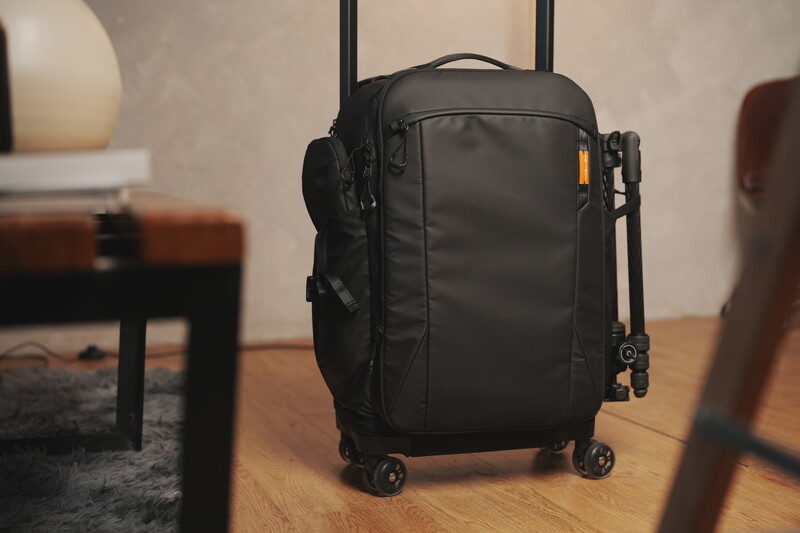Black carry-on luggage with telescoping handle positioned on wooden floor in an interior space.