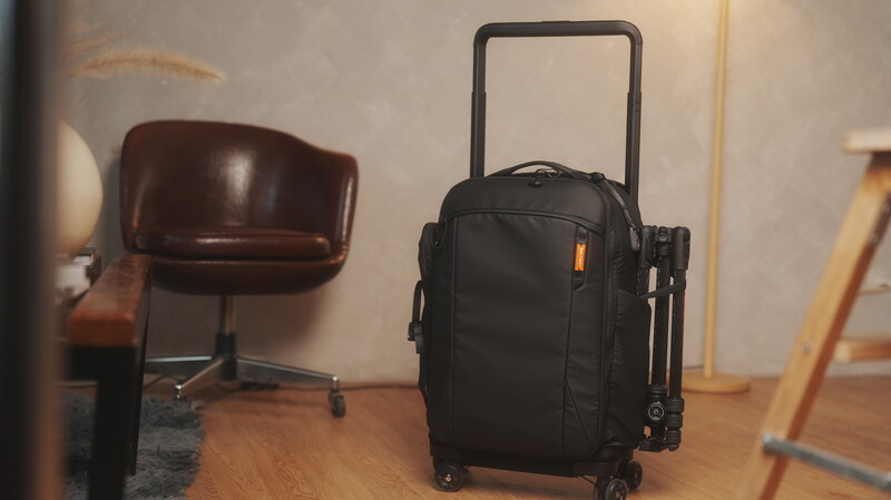 Black rolling carry-on luggage with extended handle in minimalist interior studio setting.