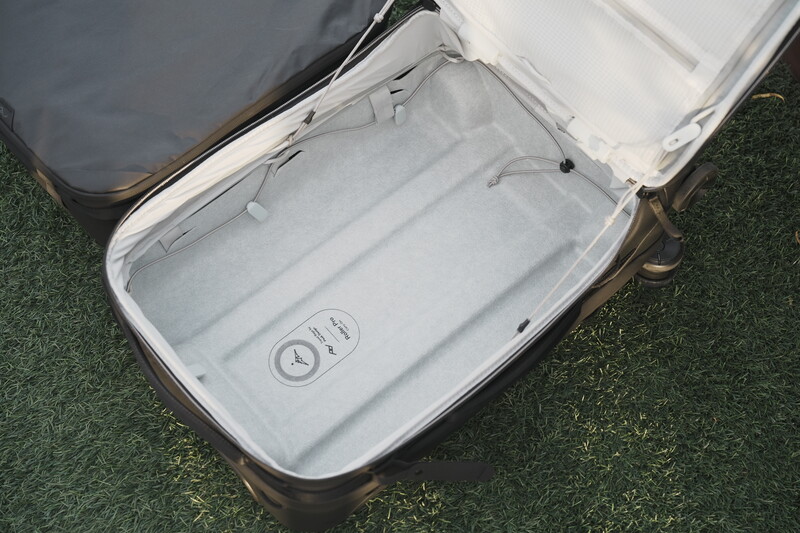 Open hardshell suitcase with light gray fabric interior lining and small circular logo emblem.